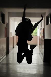 Photo by Mesh on Unsplash; silhouette of student jumping in school hallway