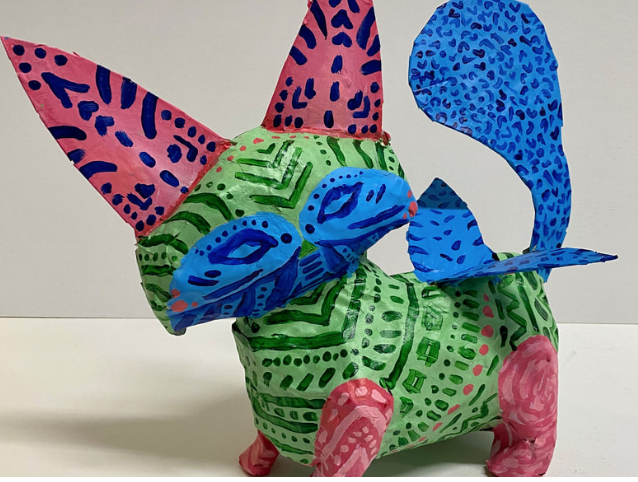 Photo of a colorful sculpture of a fantastical animal, painted in red, green, and blue. There are abstract markings of lines and dots all over the sculpture.