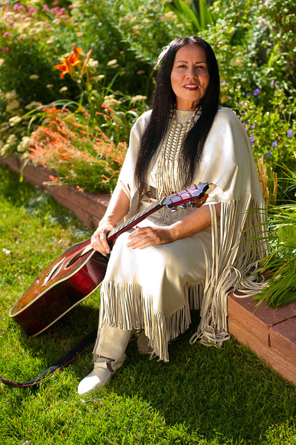 Read Feather Woman sitting down with her guitar. 
