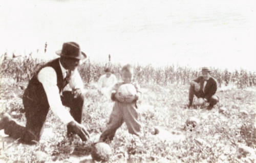 African American child holds melon as three adults watch in Dearfield, CO