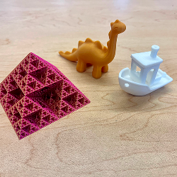 Array of small 3D printed items, from left to right: A pyramid, a dinosaur, and a boat