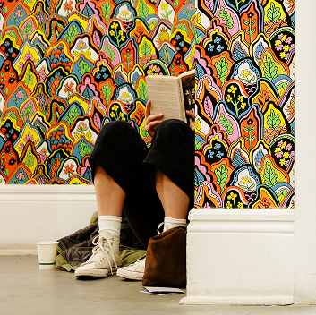 An individual reads a book in the corner of the Dikeou Collection, surrounded by colorful paisley and floral wallpaper.