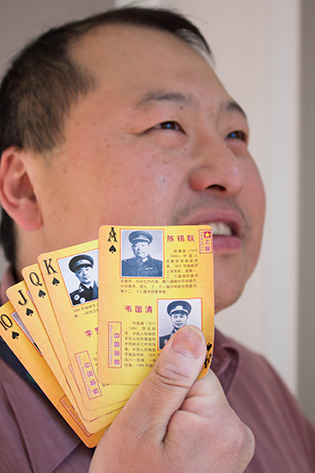 Photograph of a man holding several playing cards featuring pictures of generals and marshals on them