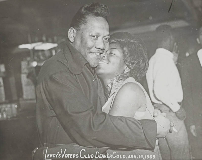 A black and white image of a Black man and woman hugging at Lerroy's Voters Club in Denver, Colorado on January 14, 1965.