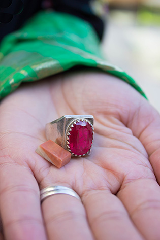 Photograph of a woman's hand holding a ring with a pink jewel and a small stone