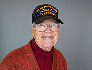 Older man wearing glasses and a "Korea - Vietnam Veteran" hat looking at the camera and smiling