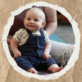 A baby smiling as he sits on his mother's lap and is read to.