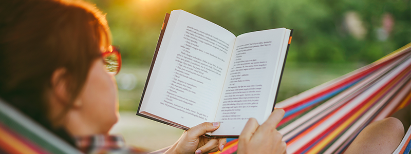 Woman reading book while resting in hammock during sunset
