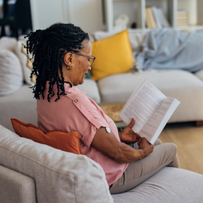 woman sitting on gray couch reading a book